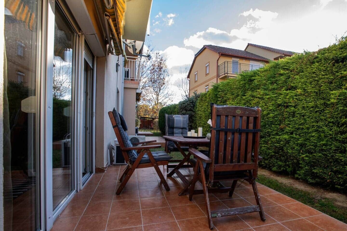 An outdoor patio with a table and chairs, a television, and a hedge.