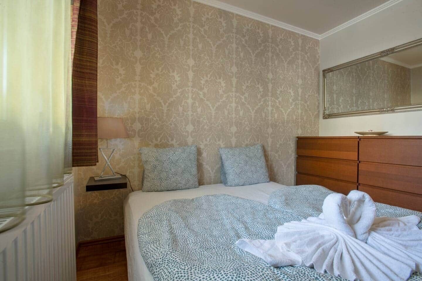 Ett hotellrum med en säng, en byrå i trä, en spegel och ett element.