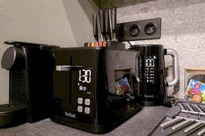 A kitchen with a coffee maker, a digital clock, and a mug. - IMCT - Urban Jungle Apartments 08 (Budapest)