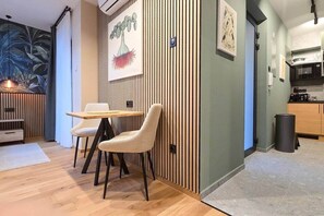 A modern interior with a dining area featuring a wooden table and two chairs, a kitchen with a microwave and cabinets, and a wall with vertical wooden slats and artwork. - IMCT - Urban Jungle Apartments 08 (Budapest)