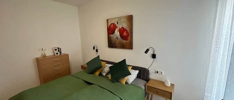 A bedroom with a bed, a dresser, a nightstand, a lamp, and a painting on the wall.