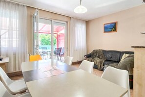 A room with a dining table, chairs, a sofa, and a painting on the wall. - LB - Horváth Vendégház 2 (Zamárdi)