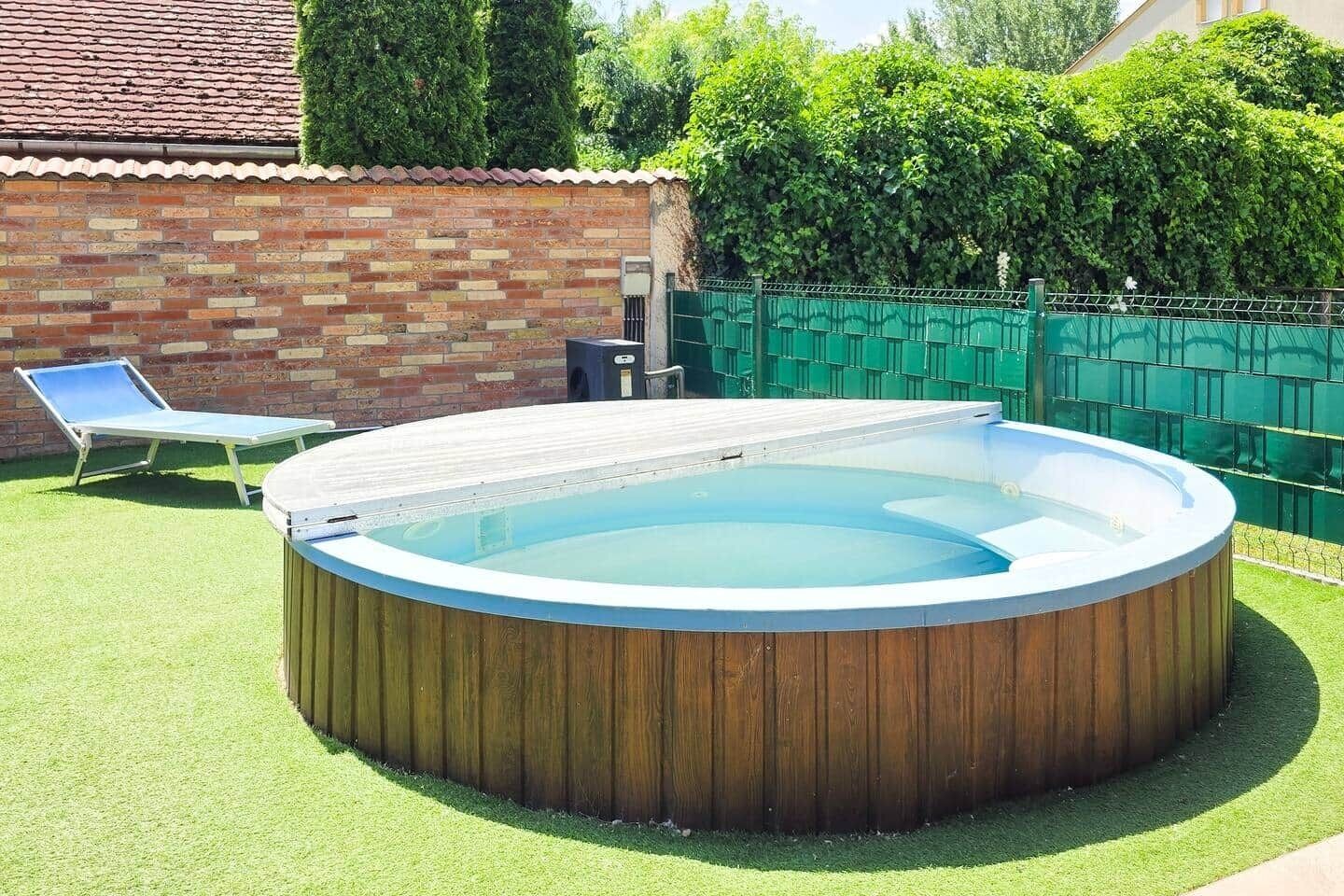 Un jacuzzi rond, avec un revêtement extérieur en bois, entouré d’une pelouse verdoyante et d’un mur en briques.