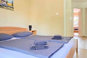 A hotel room with two beds, a nightstand, and a painting on the wall. - LB - Horváth Vendégház 2 (Zamárdi)