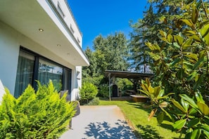 Uma casa moderna com área de estar coberta ao ar livre, calçada de acesso pavimentada e vegetação exuberante.