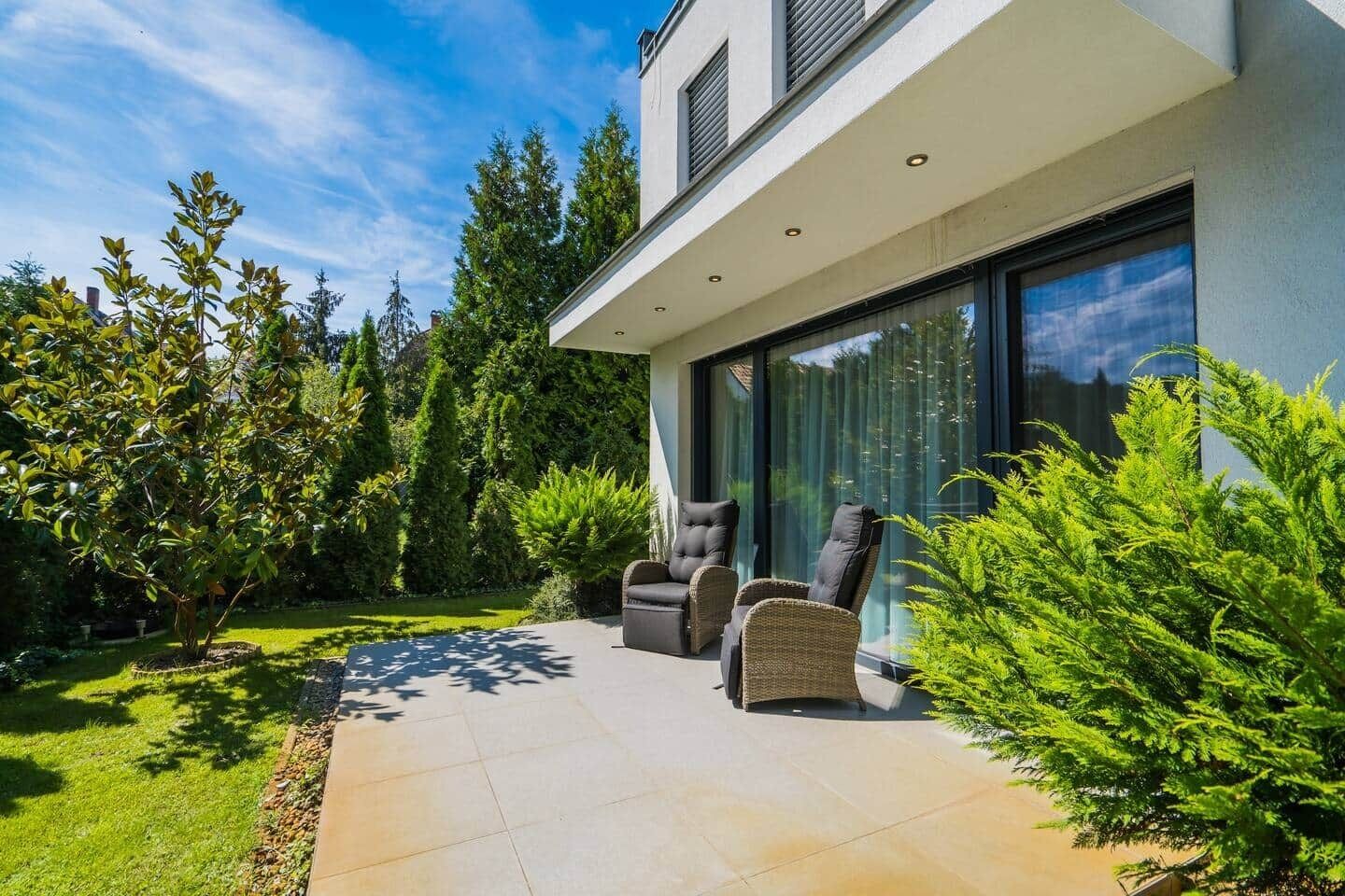 A modern house with a patio, two chairs, and a large window.
