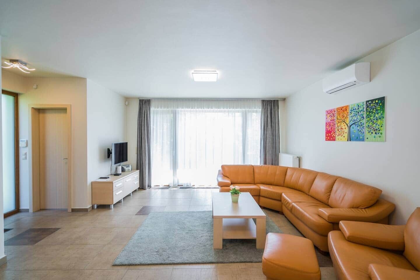 A modern living room with a sectional sofa, a flat-screen TV, a coffee table, and a large window with curtains.