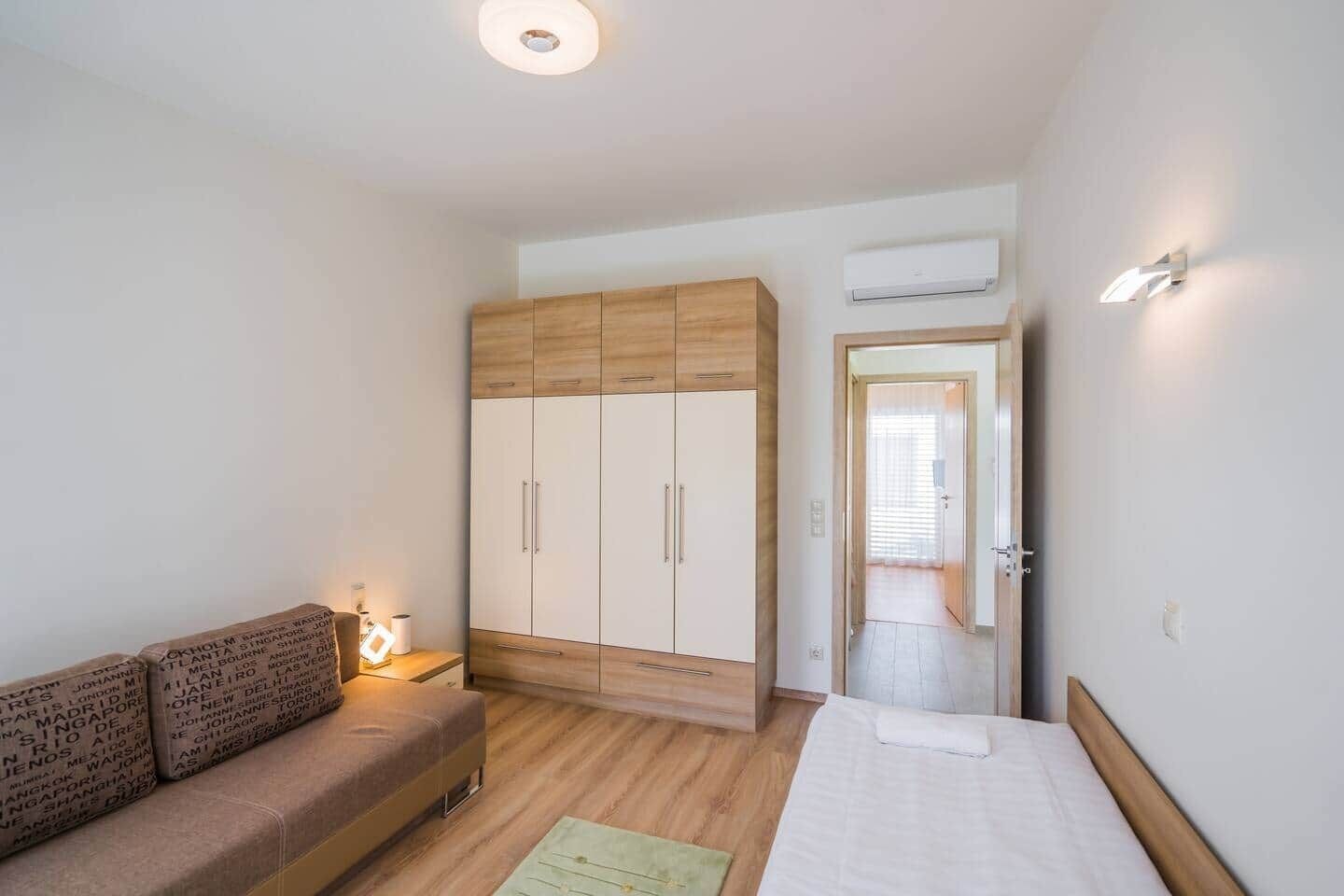 A bedroom with a bed, a wooden wardrobe, a nightstand, and a sofa.