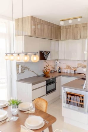A modern kitchen with wooden cabinets, a marble backsplash, and a dining area with a table set for four. - LB - LelleMarine Apartments A401 (Balatonlelle)