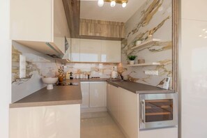A modern kitchen with a marble backsplash, a built-in oven, and a countertop with a sink. - LB - LelleMarine Apartments A401 (Balatonlelle)