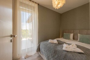 A hotel room with a bed, a headboard, a window with curtains, and a door. - LB - LelleMarine Apartments A401 (Balatonlelle)
