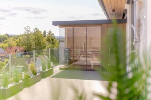 A modern building with a glass facade, a balcony with plants, and a view of the surrounding area. - LB - LelleMarine Apartments A401 (Balatonlelle)