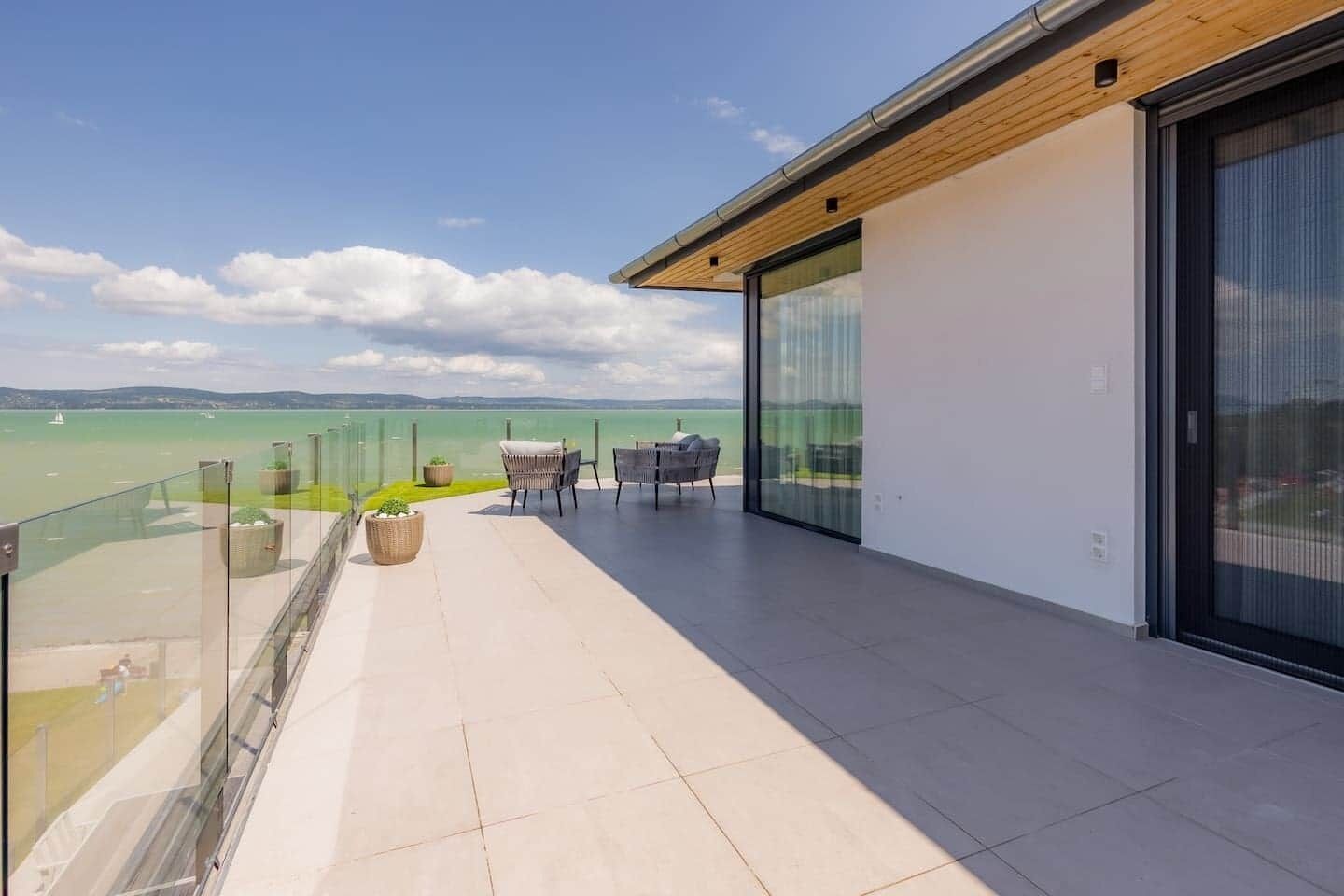 A balcony with a view of a body of water, a table with chairs, and a glass door leading to the interior.