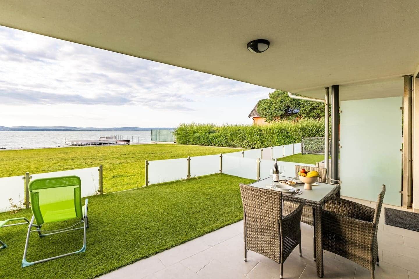 Un balcon avec une table et des chaises, une vue sur la mer et un espace verdoyant.