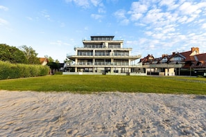 A multi-story building with a flat roof, large windows, and a grassy area in front. - LB - LelleMarine Apartments A002 (Balatonlelle)