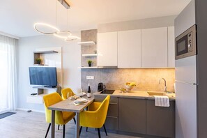 A modern kitchen with a dining area, a flat-screen TV, and a built-in oven. - LB - LelleMarine Apartments A002 (Balatonlelle)