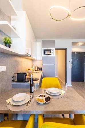 A modern dining area with a table set for two, a microwave, and a small kitchen area. - LB - LelleMarine Apartments A002 (Balatonlelle)