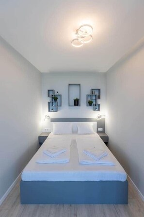 A modern bedroom with a bed, bedside tables, and wall-mounted shelves. - LB - LelleMarine Apartments A002 (Balatonlelle)