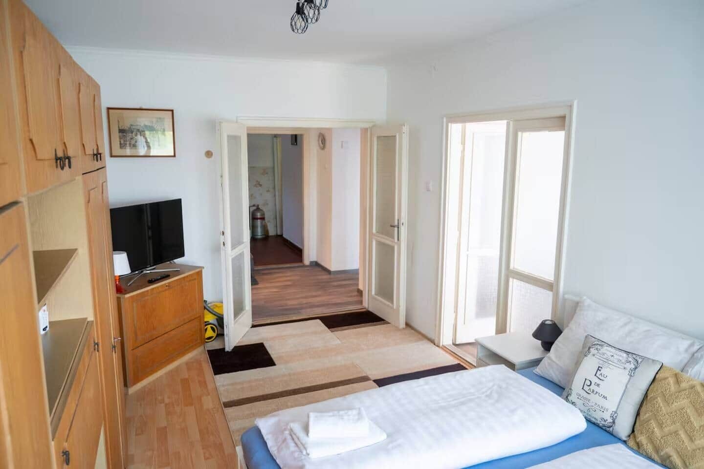 Um quarto com uma cama, televisão, guarda-roupa e corredor que dá para outro espaço.