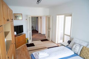 A bedroom with a bed, a television, a wardrobe, and a hallway leading to another room. - LB - Mecseki Apartman (Balatonkenese)