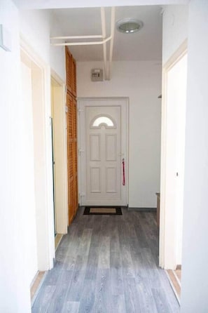 A hallway with a white door, wooden cabinets, and a grey floor. - LB - Mecseki Apartman (Balatonkenese)