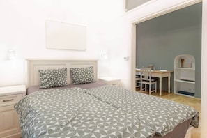 A bedroom with a bed, two pillows, a nightstand, a desk with a chair, and a shelving unit. - MidTerm - Chic Soho Apartment near Opera (Budapest)