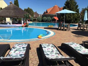 Ein Schwimmbecken mit Liegestühlen und Sonnenschirmen, umgeben von Gebäuden und Bäumen.