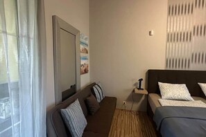 Ein Hotelzimmer mit Bett, einer Sitzecke, Nachttisch, Spiegel und einem Fenster mit Vorhängen.