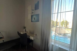 Ein Zimmer mit Schreibtisch, Stuhl und Blick auf ein Schwimmbad durch ein Fenster.