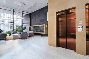 A modern lobby with a reception desk, seating area, and an elevator. - MidTerm - Rózsa 55 Apartman (Budapest)