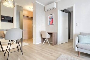 A modern living room with a sofa, a dining area with chairs, and a kitchen with an oven. - MidTerm - Rózsa 55 Apartman (Budapest)