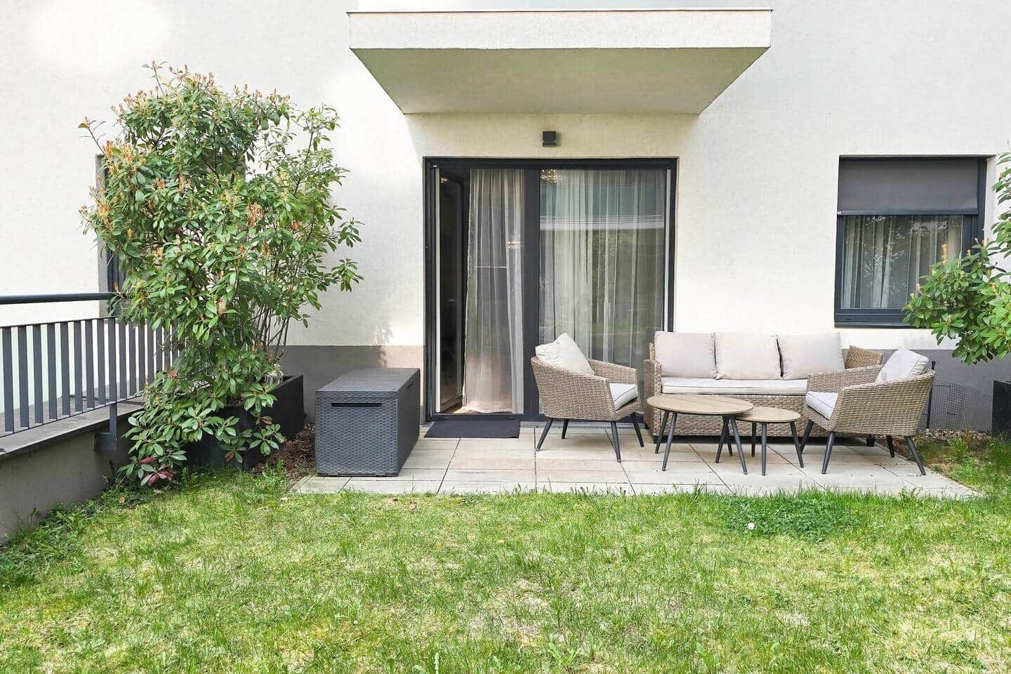 Un espace extérieur moderne aménagé avec un canapé et des fauteuils, une petite table et une plante en pot.