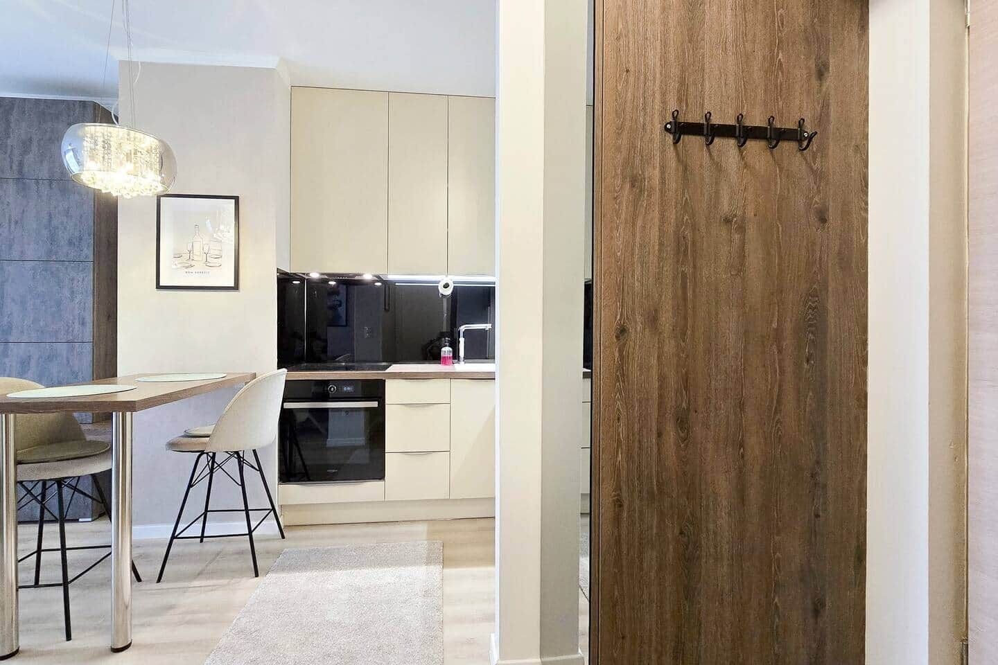 Een moderne keuken met een houten deur, een eethoek met tafel en stoelen, en een hanglamp.