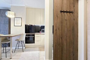A modern kitchen with a wooden door, a dining area with a table and chairs, and a pendant light. - MidTerm - Rózsa 55 Apartman (Budapest)
