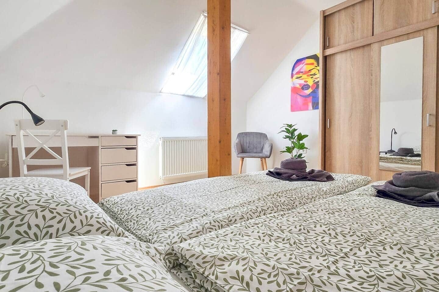 Une chambre à coucher avec un lit, un bureau, une chaise, un radiateur, une fenêtre et un tableau.