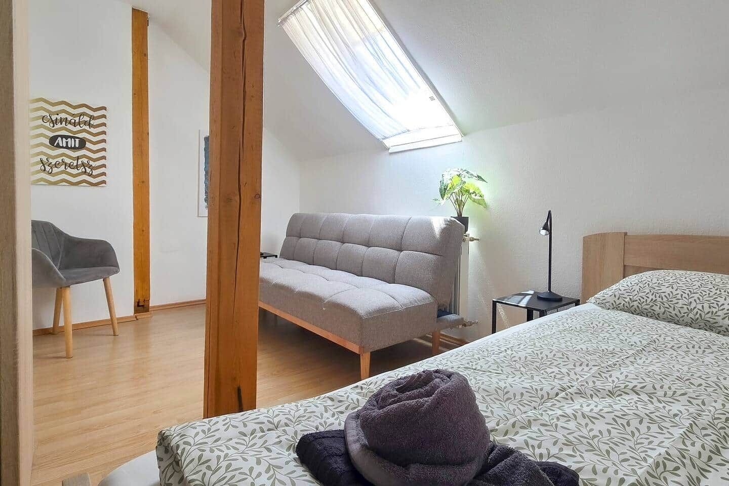Et soveværelse med seng, sofa, skrivebord og ovenlys.