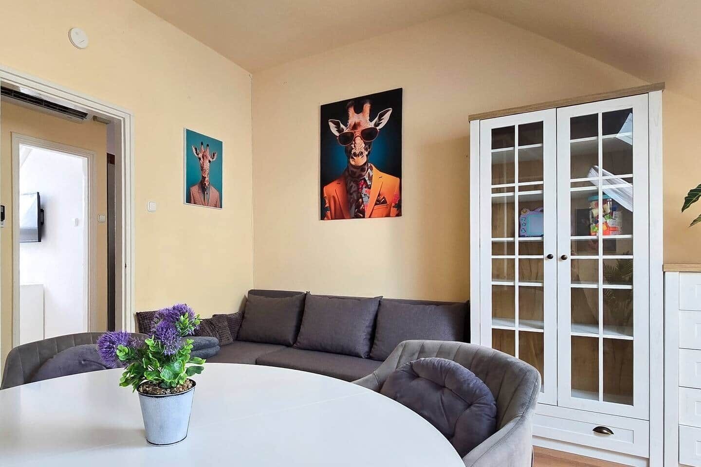 A living room with a grey sofa, a white table, and a potted plant. There are two framed pictures on the wall.