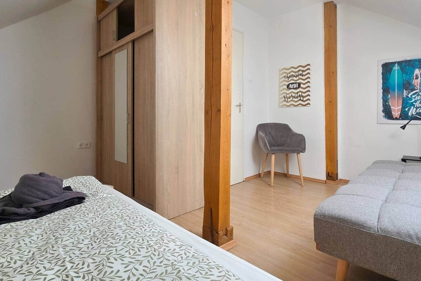 A bedroom with a bed, a chair, and a wardrobe.