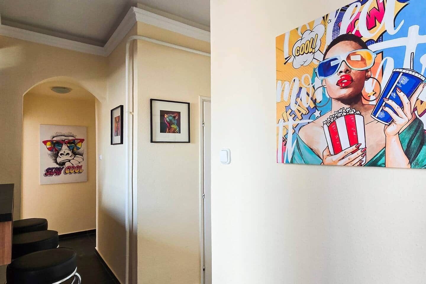 A hallway with framed artwork on the walls, a door, and a seating area with black chairs.