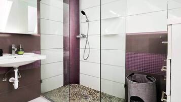Ein Badezimmer mit Dusche, Waschbecken und Mülleimer.