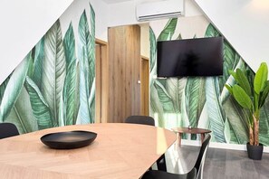 A conference room with a large table, chairs, a flat-screen TV mounted on the wall, and a large plant. - MidTerm - Rooftop Serenity Apartment 3 (Budapest)