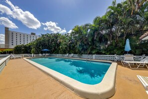 A rectangular pool with a white deck edge, surrounded by palm trees and a white fence.