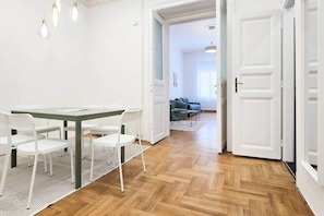 A room with a dining table, chairs, a patterned rug, and a wooden floor. - MidTerm - CityCenter67 Apartment (Budapest)