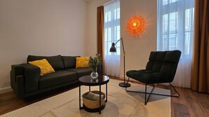 Een woonkamer met een donkergroene bank, een ronde salontafel, een vloerlamp en een moderne lamp.