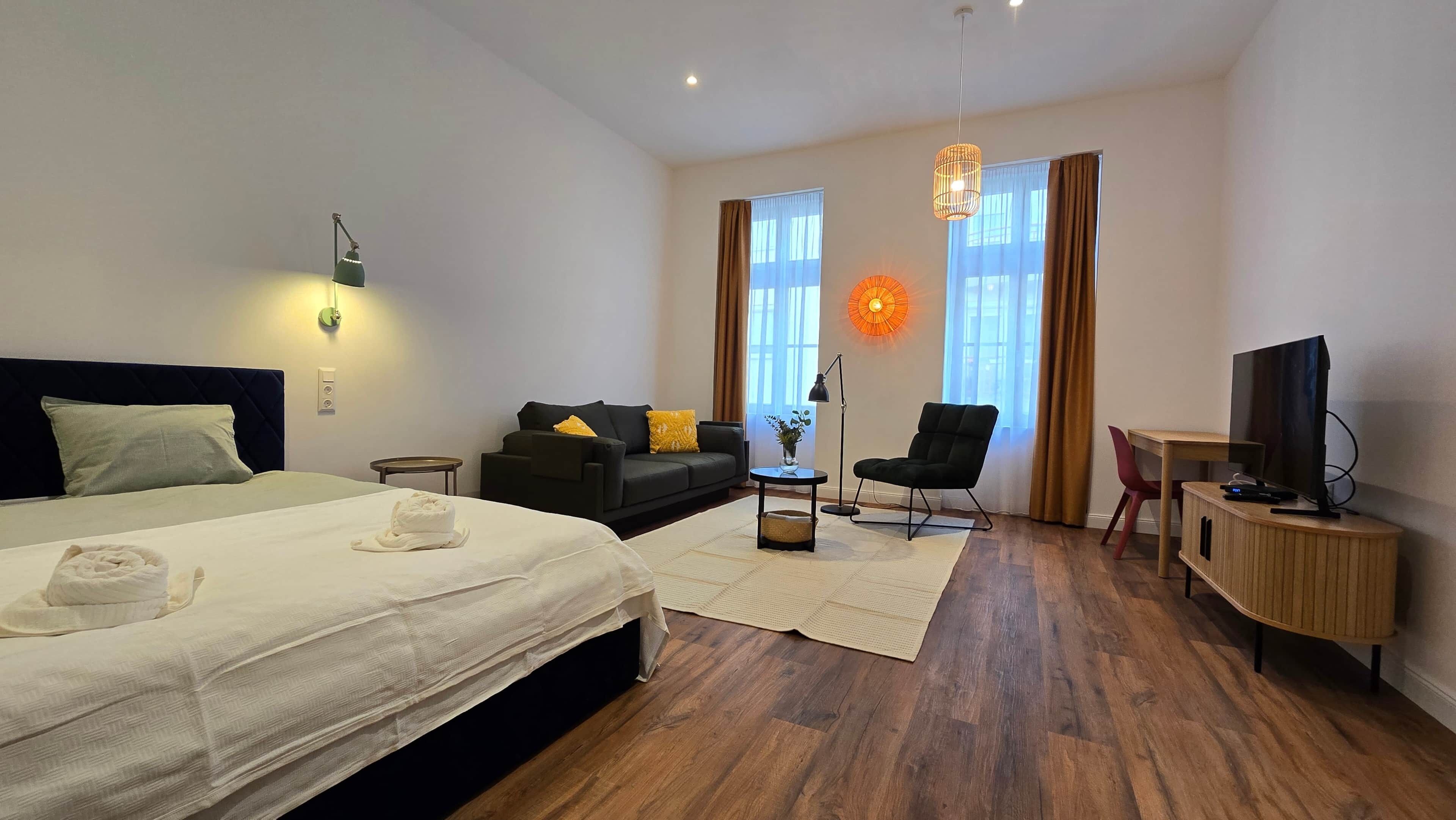A hotel room with a bed, a sofa, a chair, a TV, and a desk.