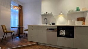 Eine moderne Küche mit eingebautem Geschirrspüler, einer kleinen Essecke mit rundem Tisch und zwei Stühlen sowie einem Fenster mit durchsichtigen Vorhängen.