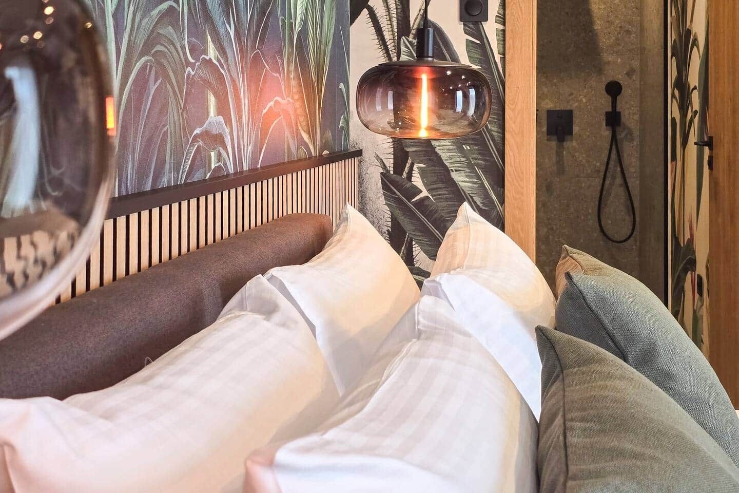 Ein Bett mit weißer und grauer Bettwäsche, ein Holz-Kopfteil und eine Wand mit einer großen Pflanzen-Mural.