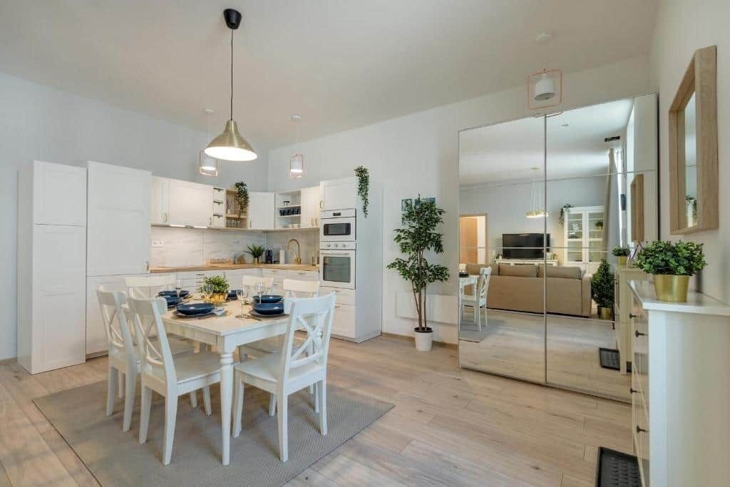 A modern kitchen with white cabinetry, a dining table with chairs, and a large mirror reflecting the room.