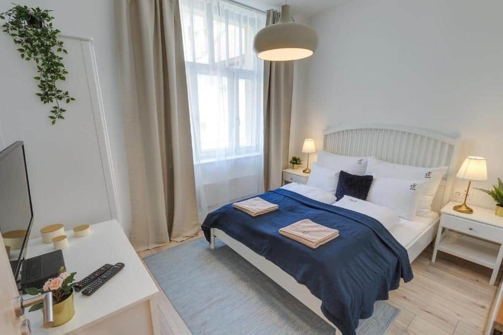 A hotel room with a bed, bedside tables, a desk with a computer, and a window with curtains.