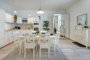 A modern kitchen with white cabinetry, a dining table set for four, and pendant lighting. - MidTerm - Rózsa Apartments - Mira (Budapest)